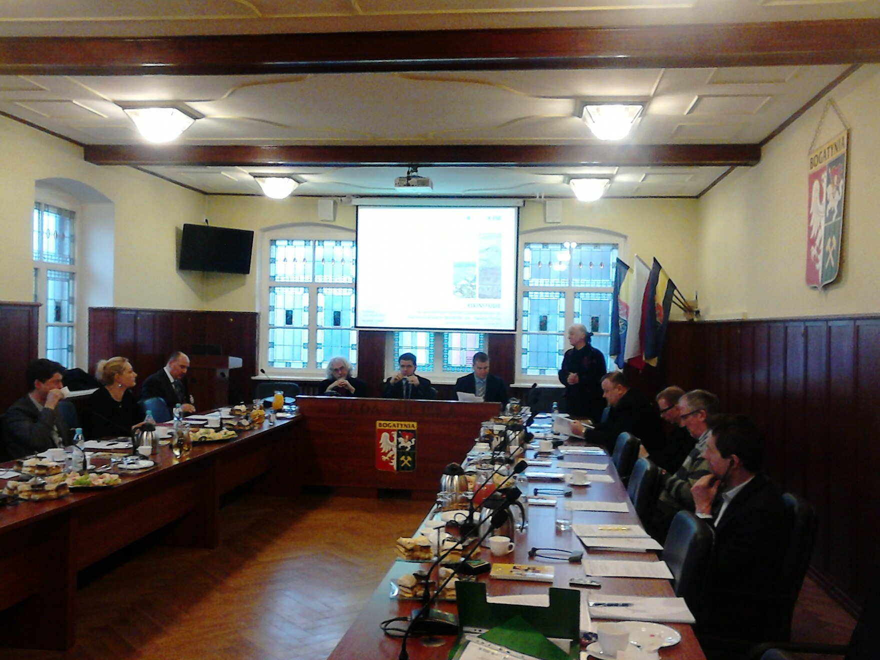 Blick in den Konferenzraum, Teilnehmer sitzen im Karee. Frau Diersch, Sächsisches Staatsministerium des Innern spricht von Ihrem Platz die Teilnehmer an.