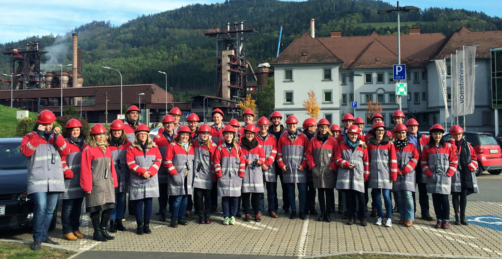 Alle Teilnehmer*innen der Auftaktkonferenz zum Projekt InduCult2.0 während einer Exkursion zum Unternehmen Voest Alpine in Leoben, Österreich aufgereiht vor dem Betriebsgelände des Unternehmens.